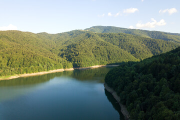 Aerial view of big lake with clear blue water between high mountain hills covered with dense evergreen forest.