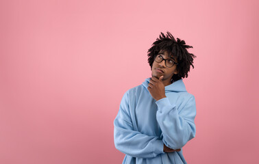 Pensive Afro teen guy touching his chin, thinking over something on pink studio background, copy...