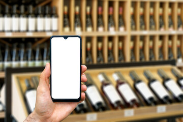 Wine shop with bottles background. Hand with blank smartphone screen one wine backdrop. Buying and...