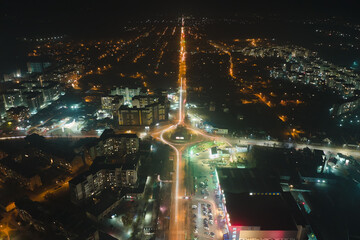 Aerial view of high rise apartment buildings and bright illuminated roundabout intersection on urban street in city residential area at night. Dark urban landscape