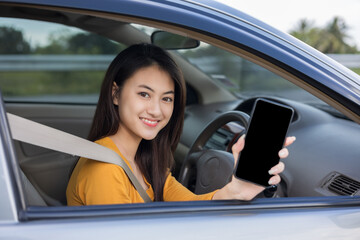 Fototapeta na wymiar Young Asian woman smiling drives a beautiful nature on the road. She showing blank screen smartphone. Female using cell phone navigation for driving location