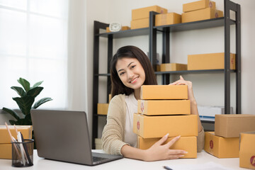 Young beautiful asian entrepreneur stacking the parcel cardboard and hugging product and smile to camera. Happy business woman with many box working at home. Small business owner start up concept.