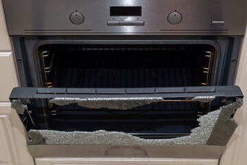 Obraz premium Opened broken oven door in the kitchen, top view, close-up. Broken glass from overheating. Broken glass from impact. Warranty repair. Repair of electric stoves and ovens