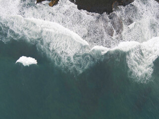 Top down aerial view of giant ocean waves crashing and foaming in coral beach