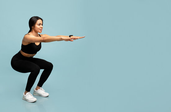 Fitness and sport. Slim african american lady doing deep squat exercises, working out over blue background, empty space