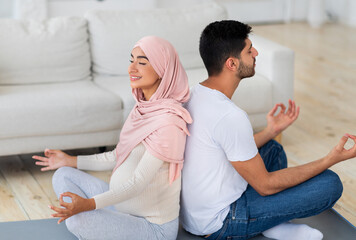 Yoga for pregnancy. Happy muslim spouses meditating together at home, sitting back to back and...
