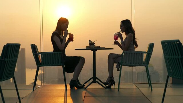 4K Beautiful Asian woman friends meeting and dinner party together at skyscraper rooftop restaurant in metropolis at summer sunset. Female friend enjoy outdoor lifestyle activity in the city at night