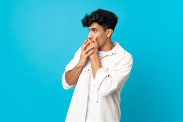 Young Argentinian man isolated on background covering mouth and looking to the side