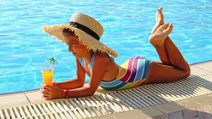 The child is drinking a cocktail by the pool. Selective focus.