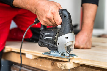 Close up on hand of unknown carpenter working with an electric jigsaw cutting wood with saw...
