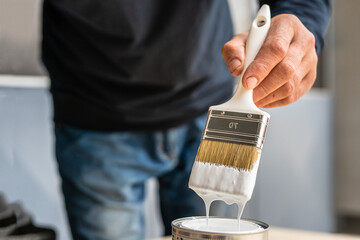 Close up on white paint brush in the hand of unknown man hobby painting and renovation repairing...