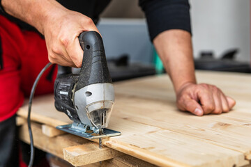 Close up on hand of unknown carpenter working with an electric jigsaw cutting wood with saw woodworking hobby concept copy space