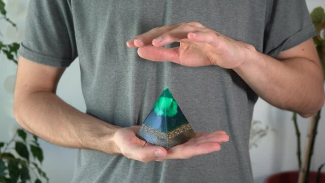 Man feeling the energies of green orgonite pyramid. Close-up.