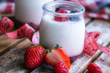 yogurt with wild berries and measuring tape. diet and eating concept