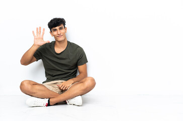 Young Argentinian man sitting on the floor counting five with fingers