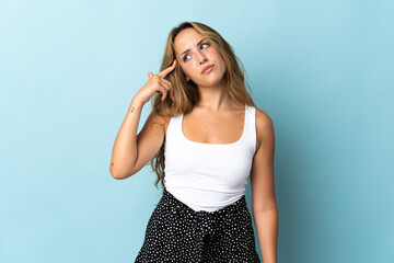 Young blonde woman isolated on blue background making the gesture of madness putting finger on the...