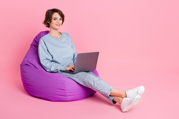 Full length photo of nice millennial lady sit work latop modern technology wear sweatshirt jeans footwear isolated on pink background