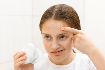 face of a teenage girl with pimples, she looks at herself in the mirror and takes care of her skin,...