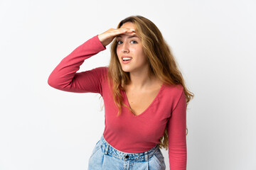 Young blonde woman isolated on blue background looking far away with hand to look something