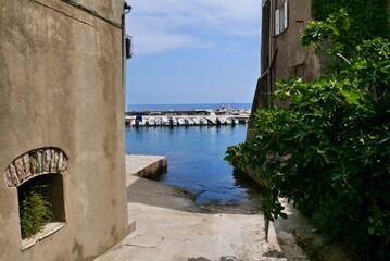 Fototapeta na wymiar View of fishing harbor of Erbalunga through narrow alleyway. Cap Corse, Corsica, France.