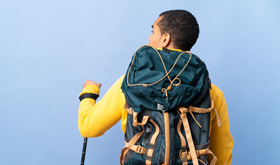 African American man with backpack and trekking poles over isolated background in back position and...
