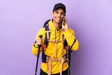 African American man with backpack and trekking poles over isolated background keeping a conversation with the mobile phone with someone