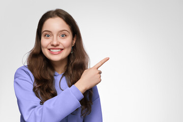 A young woman with long hair and blue eyes points her finger to the right side. The girl is wearing...
