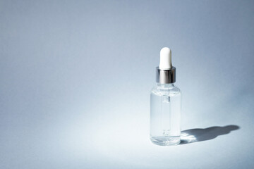 Transparent glass bottle with silver and white pipette in light on grey background mockup. Facial...
