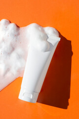 Plastic white tube and the appearance of the texture of the foam on an orange background. Skincare cleansing cosmetic in top view. Beauty concept for face body care