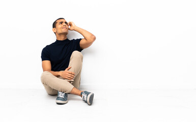 Fototapeta premium African American man sitting on the floor having doubts and with confuse face expression