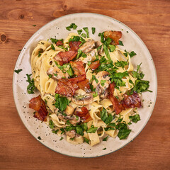 Fettuccine pasta with creamy mushroom sauce, fried bacon and parsley - portion in a plate, close-up, top view