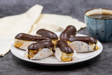 Tasty eclairs and cup of coffee on dark table. Traditional french dessert. Pastry products. Close up