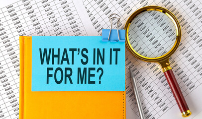 WHAT'S IN IT FOR ME text on sticker on notebook with magnifier and chart. Business concept