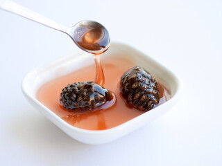 Pine cones jam in bowl, in spoon isolated on white background, on table.