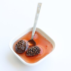 Pine cones jam in bowl, in spoon isolated on white background, on table. Top view.
