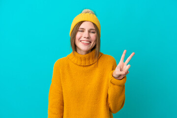 Fototapeta premium Young English woman wearing winter jacket isolated on blue background smiling and showing victory sign