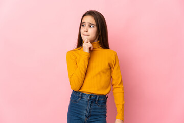 Little girl isolated on pink background having doubts and thinking