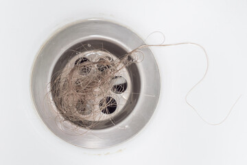 A bundle of blonde women's hair was left in the bathroom drain after taking a shower. Close-up, top view. The problem of hair loss. - obrazy, fototapety, plakaty