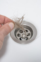 A man's hand cleans a bathtub drain from a bundle of blond hair. Close-up. The problem of hair loss.