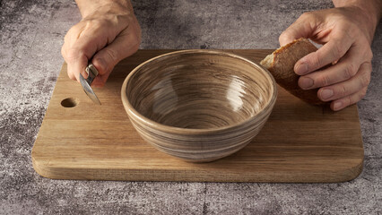 old man's hands clutching a piece of bread and a spoon over an empty bowl, poverty concept