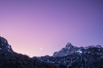 Crescent waning moon in purple sky overy mountain peaks