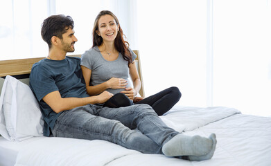 Caucasian husband lies down on belly of pregnant wife on bed at home to embrace unborn baby and...