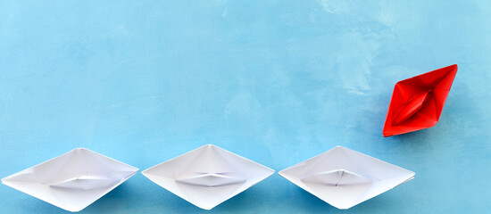 The concept of leadership. The red flagship paper ship leads the others ahead on a blue background.