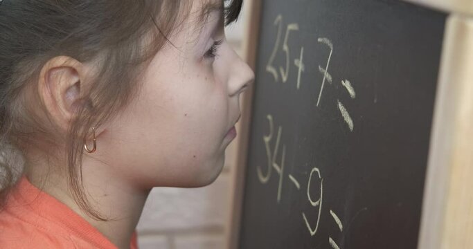 Write on blackboard the math. A view of pensive child with maths on blackboard in the room.