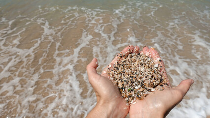 The girl holds a large sea sand in her hands against the background of the sea surf. Wet sand. Close-up. The concept of recreation, tourism and travel.
