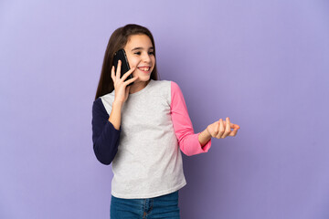 Little girl isolated on purple background keeping a conversation with the mobile phone with someone