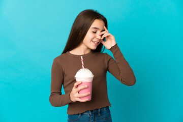 Little girl with strawberry milkshake isolated on blue background laughing