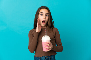 Little girl with strawberry milkshake isolated on blue background with surprise and shocked facial...