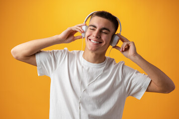 Handsome teenage boy with headphones on head against yellow background