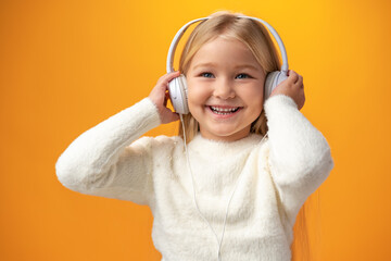 Little girl child wear headphones listen to music over yellow background